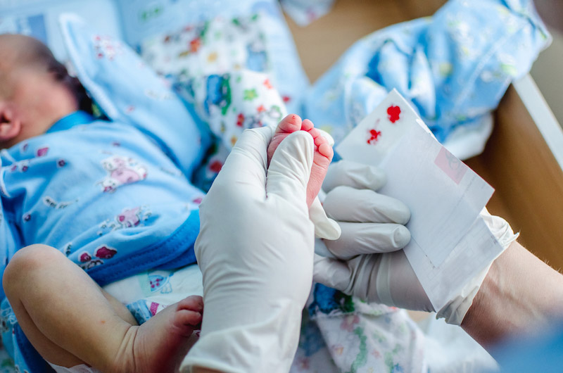 Primo piano del piede di un neonato mentre l'infermiera esegue un prelievo di sangue dal tallone per lo screening neonatale