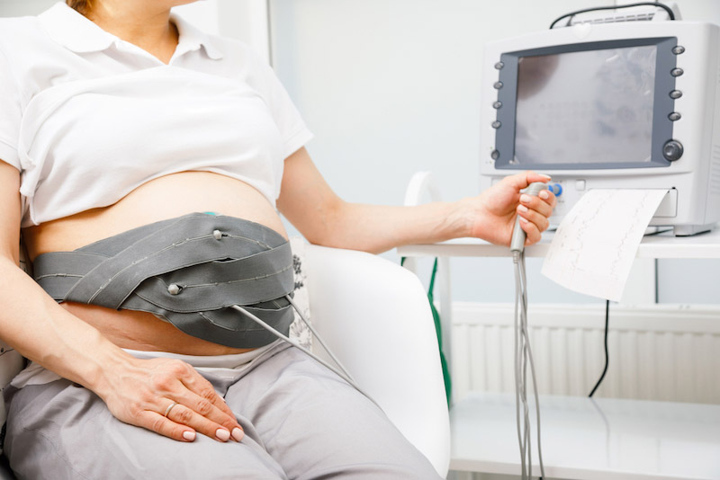Primo piano della pancia di una donna in gravidanza con strumentazione per seguire una cardiotomografia