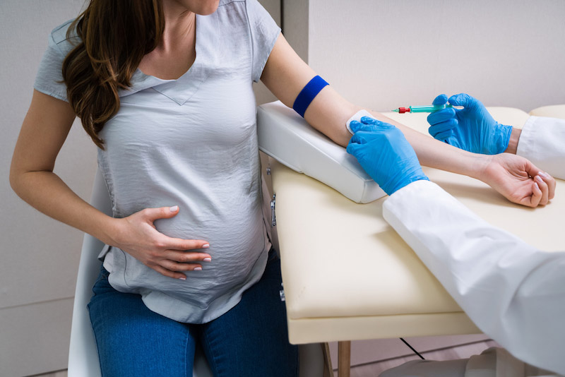 Donna gravida seduta in una sala visita mentre l'infermiere esegue il prelievo del sangue per il tri-test