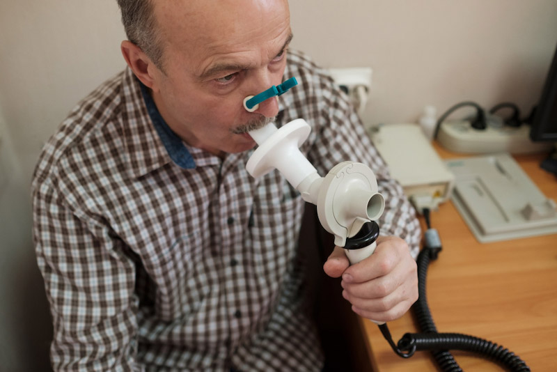 Paziente seduto su una sedia in una stanza ambulatoriale con uno stringinaso e un boccaglio collegato allo spirometro per eseguire la spirometria 