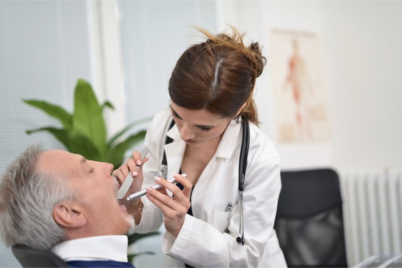 Dottoressa osserva la gola di un paziente seduto in una sala ambulatoriale