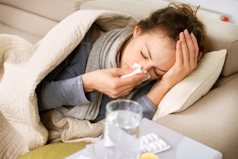 Donna sdraiata su un divano sta male e si soffia il naso a causa dell'influenza