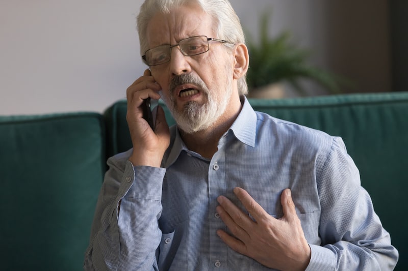 Primo piano di un uomo che chiama aiuto al telefono mentre mette la mano al petto a causa di uno shock cardiogeno