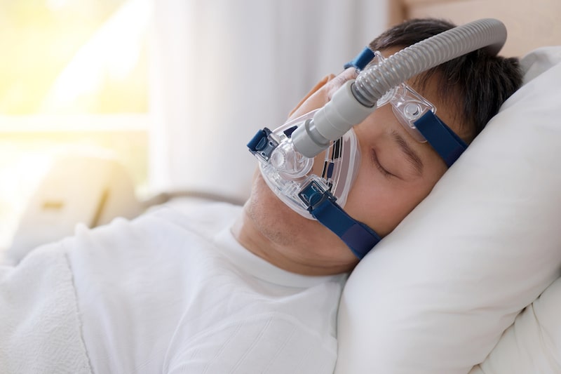 Primo piano di un uomo sdraiato a letto che dorme mentre indossa un CPAP per la trattare l'apnea del sonno