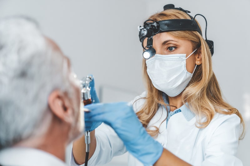 Otorinolaringoiatra esamina le cavità nasali di un paziente uomo seduto nello studio medico