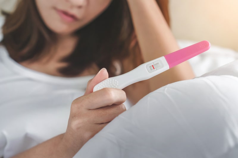 Primo piano di un test di gravidanza negativo e sullo sfondo una donna infertile