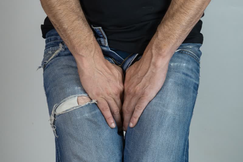 Uomo vestito con jeans strappati che si tiene le mani intorno alla zona genitale affetto da condiloma