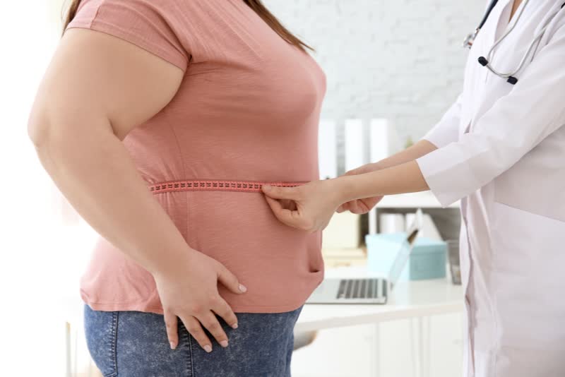 Donna sovrappeso mentre viene eseguito un test di misurazione del girovita da un medico o infermiere per rappresentare l'obesità