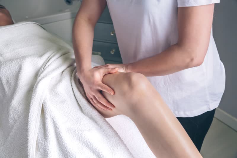 Terapeuta che massaggia la gamba di una paziente distesa su lettino per effettuare un linfodrenaggio manuale