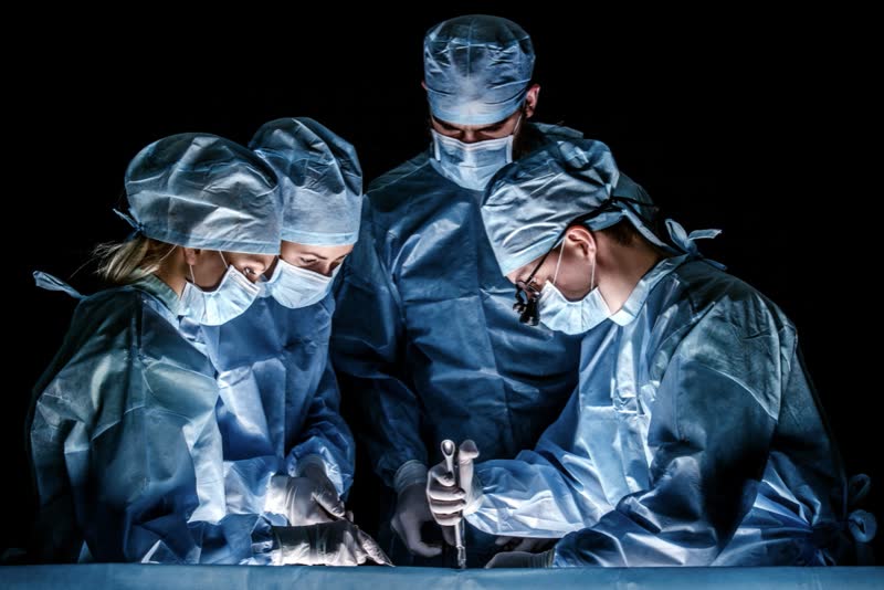 Equipe medica su sfondo scuro pronta ad intervenire su un paziente per effettuare una sternotomia