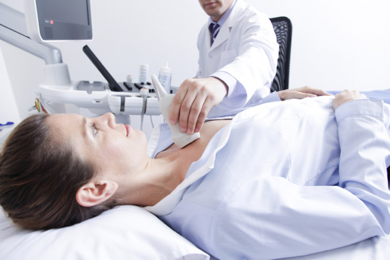 Primo piano di una paziente donna sdraiata su un lettino mentre il medico scorre una saponetta ad ultrasuoni sul torace della donna per eseguire un Ecocardiocolordoppler