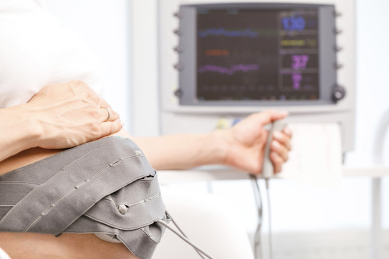 Primo piano della pancia di una donna in gravidanza avvolta da una fascia collegata all'apparecchiatura per eseguire una ecocardiografia fetale 