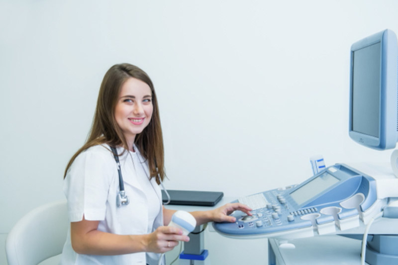 Giovane medico sorridente, che utilizza la macchina per la scansione a ultrasuoni per eseguire un ecodopler