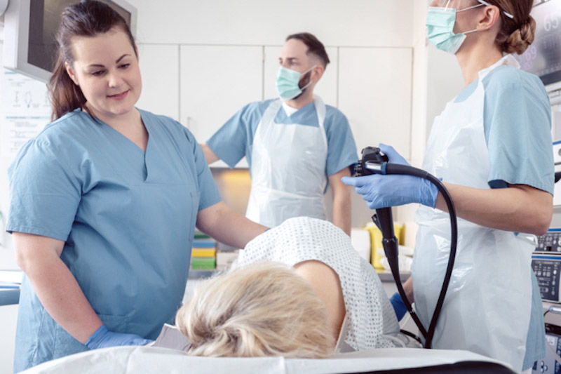 Paziente sdraiato sul lettino ed equipe di medici in ospedale durante la sigmoidoscopia 