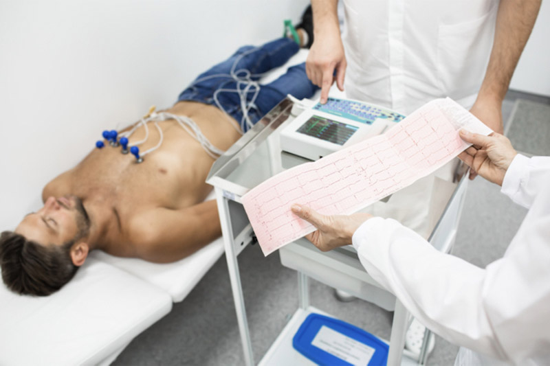 Medico tiene i risultati dell'elettrocardiogramma di un giovane paziente sdraiato su un letto d'ospedale per indagare su possibile presenza di tachicardia 