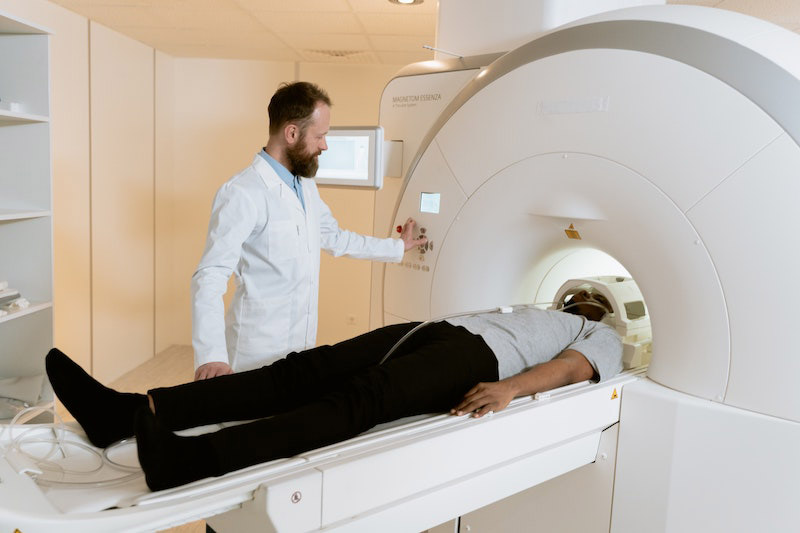 Paziente sdraiato sul lettino della tomografia computerizzata mentre il medico accanto attiva la macchina
