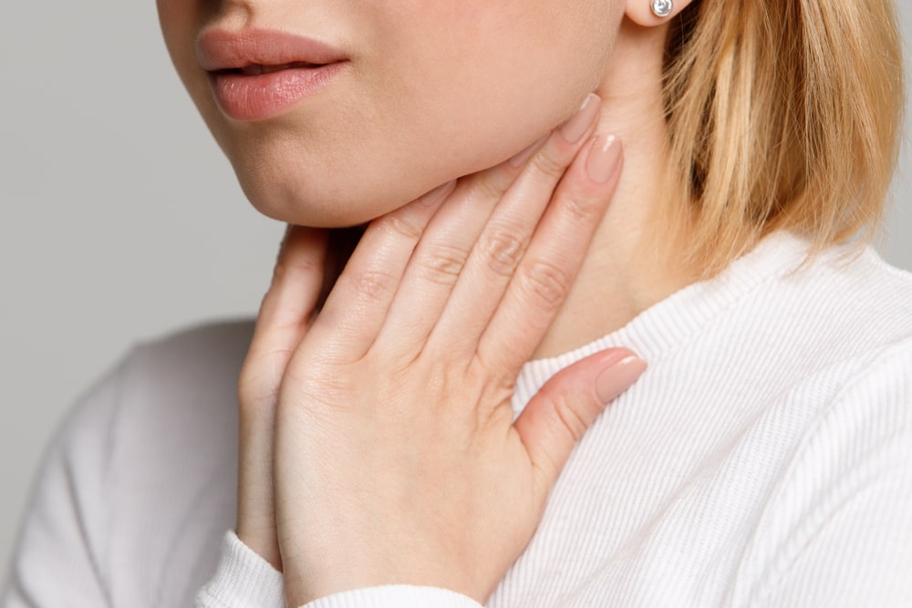 Primo piano della volto di una donna che si mette le mani al collo per dolore a causa della laringite