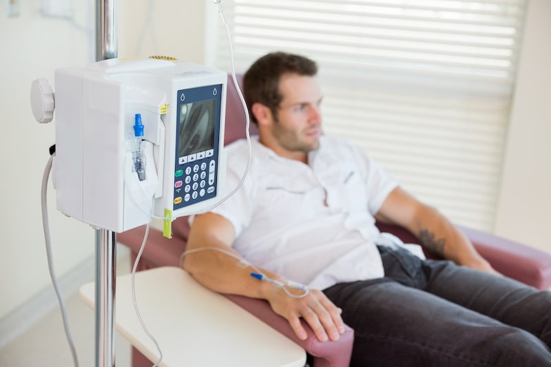 Uomo adulto sullo sfondo seduto in una sala di ospedale mentre svolge la chemioterapia