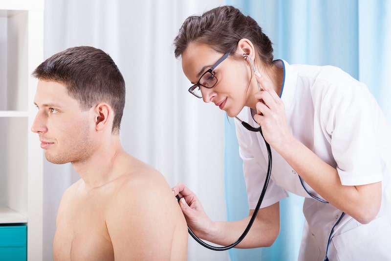 Paziente maschio viene auscultato da un medico donna mediante stetoscopio