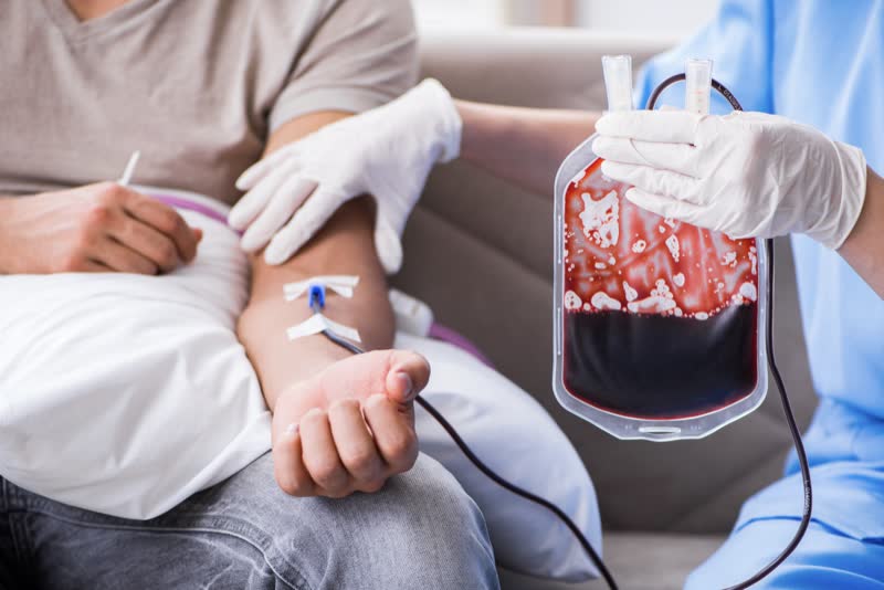 Immagine di dottore con in mano sacca di sangue collegata al braccio di un paziente nel corso di una trasfusione di sangue per curare anemia