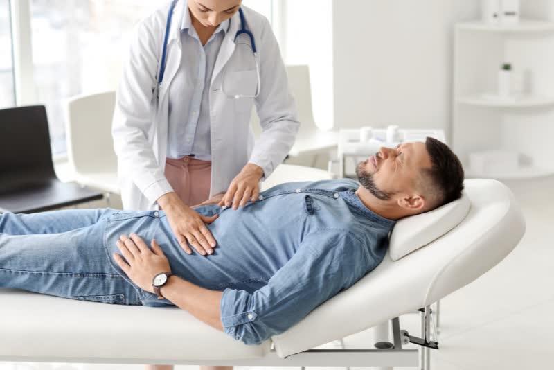 Foto di dottoressa che tasta l'addome di un paziente dolorante steso su un lettino all'interno di un ambulatorio poiché sofferente di gastroenterite