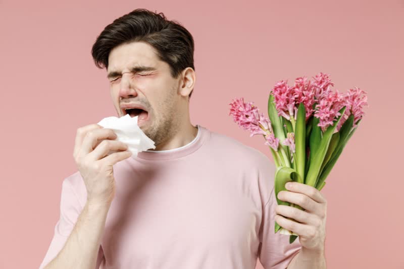 Foto di ragazzo che starnutisce con mazzo di fiori in mano per rappresentare la rinite allergica (o febbre da fieno)