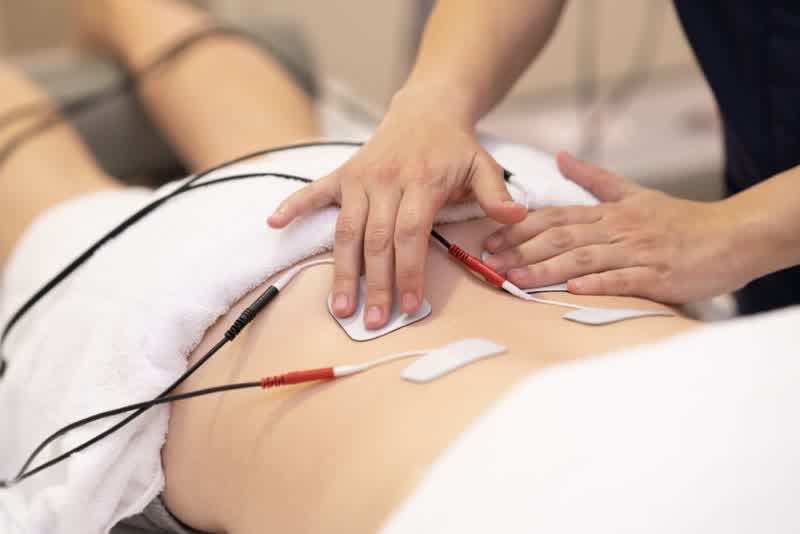 Fisioterapista che applica elettrodi per l'elettrostimolazione per svolgere una terapia fisica sulla schiena di una giovane donna