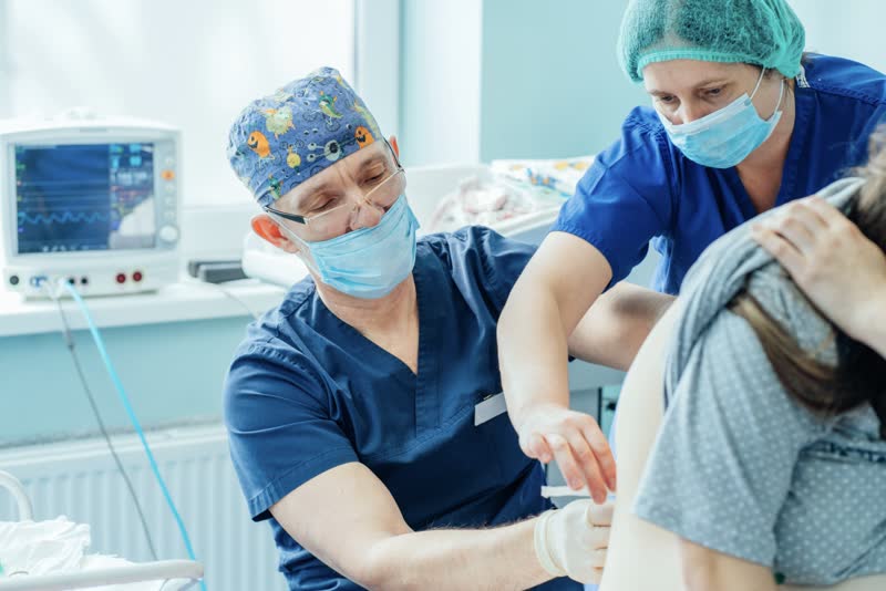 Infermieri vestiti con camici blu che effettuano una puntura per partoanalgesia su una paziente